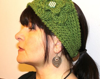 May include: A green knitted headband with a white and blue striped button. The headband is worn by a person with dark hair and a silver earring.