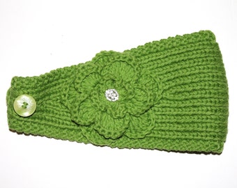 May include: Green knitted headband with a large crocheted flower and a button. The flower has a rhinestone in the centre.