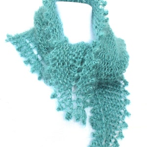 Könnte beinhalten: Türkisfarbener, handgestrickter Schal mit zartem, offenem Gewebe. Der Schal hat einen gewellten Rand mit kleinen, dekorativen Bommeln. Die weiche, flauschige Textur und das einzigartige Design machen ihn zu einem stilvollen Accessoire.
