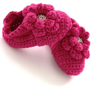 May include: A pair of pink crocheted baby booties with a flower design and a rhinestone embellishment.