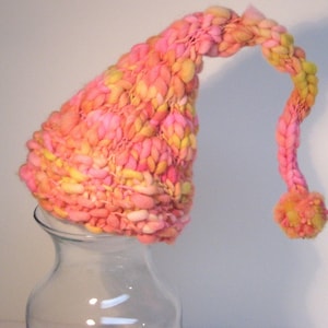 May include: A pink and yellow knitted hat with a long, curled brim and a pom-pom on the end.