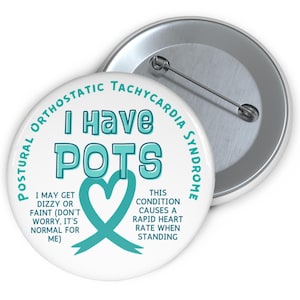 May include: A white button with a teal ribbon and heart. The text on the button reads "I Have POTS" and "Postural Orthostatic Tachycardia Syndrome". The text also says "This condition causes a rapid heart rate when standing" and "I may get dizzy or faint (don't worry, it's normal for me)".