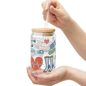 May include: A clear glass water bottle with a bamboo lid and a straw. The bottle is decorated with a colorful cartoon design featuring a heart, a stethoscope, a bandage, and socks.