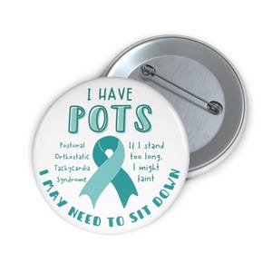 May include: White button with teal text and ribbon design. Text reads "I HAVE POTS" and "I MAY NEED TO SIT DOWN". The button also lists symptoms of Postural Orthostatic Tachycardia Syndrome.