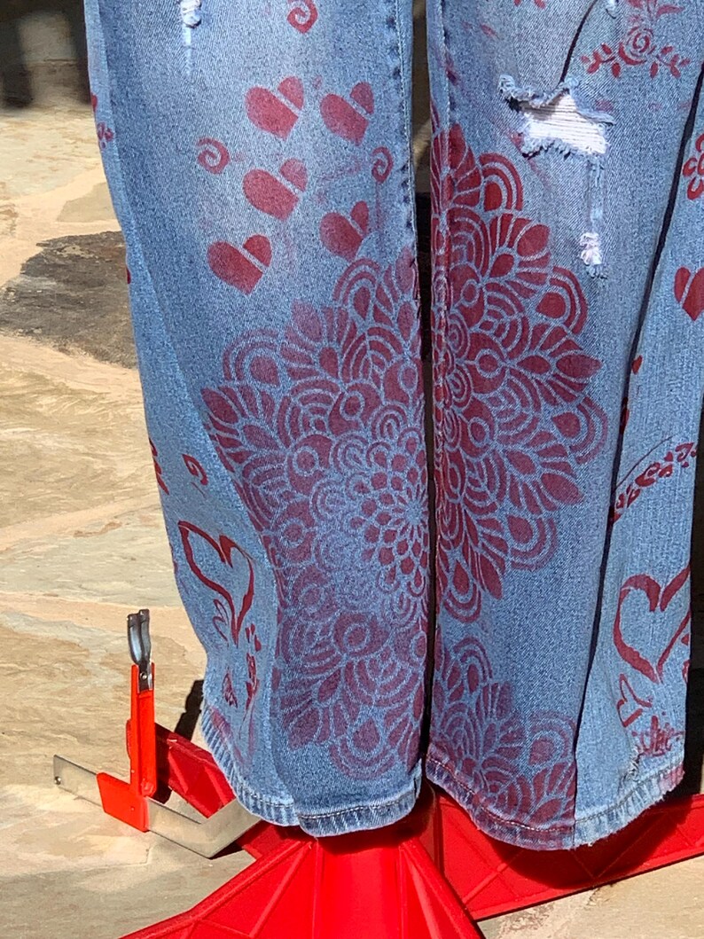 View the light distressing, red mandala stenciling, roses, garlands and the word "love" near the hem line.