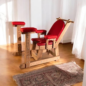 May include: A wooden chair with red upholstery and armrests. The chair has a tall backrest and is supported by four legs. The chair is on a wooden floor with a rug underneath.