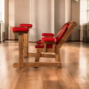 May include: A wooden chair with red upholstery and armrests. The chair is on a wooden frame with a footrest. The chair is in a room with a wooden floor.