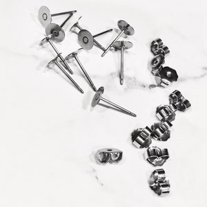 May include: A close-up of a set of silver earring backs and earring posts. The earring backs are butterfly style and the earring posts have a flat disc on the end.