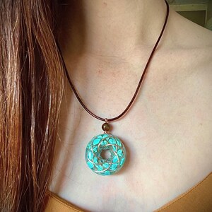 May include: A turquoise blue pendant necklace with a copper wire design. The pendant is round and has a small brown bead at the top. The necklace is made of brown leather cord.