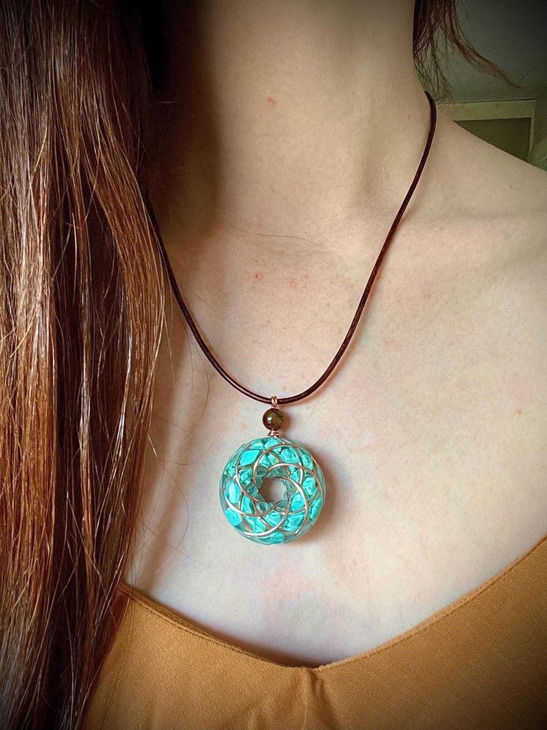May include: A turquoise blue pendant necklace with a copper wire design. The pendant is round and has a small brown bead at the top. The necklace is made of brown leather cord.