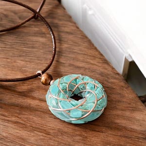 May include: A turquoise blue glass pendant necklace with a copper wire design. The pendant is round and has a spiral pattern. The necklace is made with a brown leather cord.