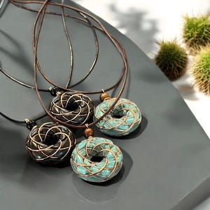 May include: Three necklaces with intricate ceramic pendants. The pendants are in the shape of a circle with a woven design. One pendant is black, one is turquoise, and one is a mix of black and turquoise.