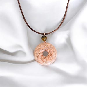 May include: A rose quartz pendant necklace with a copper wire design and a tiger's eye bead. The necklace is on a brown leather cord.