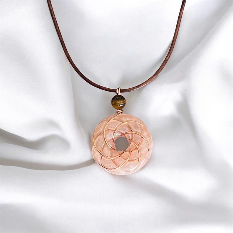 May include: A rose quartz pendant necklace with a copper wire design and a tiger's eye bead. The necklace is on a brown leather cord.