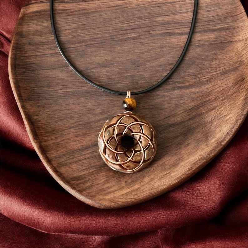 May include: A brown wooden pendant with a geometric design hangs from a black leather cord. The pendant is accented with a tiger's eye stone.