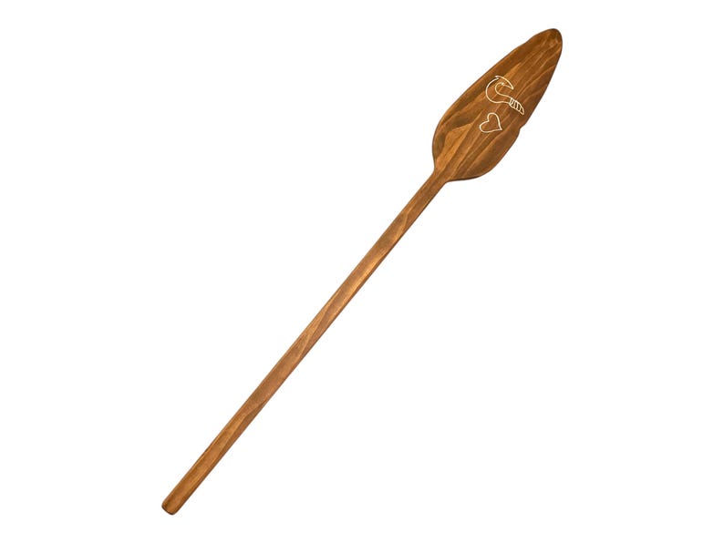 Op de afbeelding: Een houten peddel met een gesneden ontwerp van een vogel en twee harten. De peddel is bruin en heeft een lange steel.