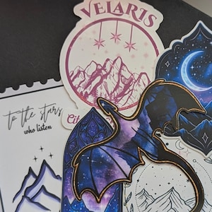 May include: A collection of five stickers featuring fantasy-themed illustrations. Designs include a dragon silhouette, mountain ranges, a crescent moon, and text reading "Velaris," "City of Starlight," and "To the stars who listen" in various fonts.