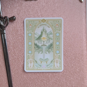 Puede incluir: Una pegatina rectangular con una ilustración central de una espada, una corona y un libro abierto bajo un castillo, con el texto "to whatever end" arqueado encima. El diseño incluye detalles en verde, dorado y azul sobre una superficie oro rosa.