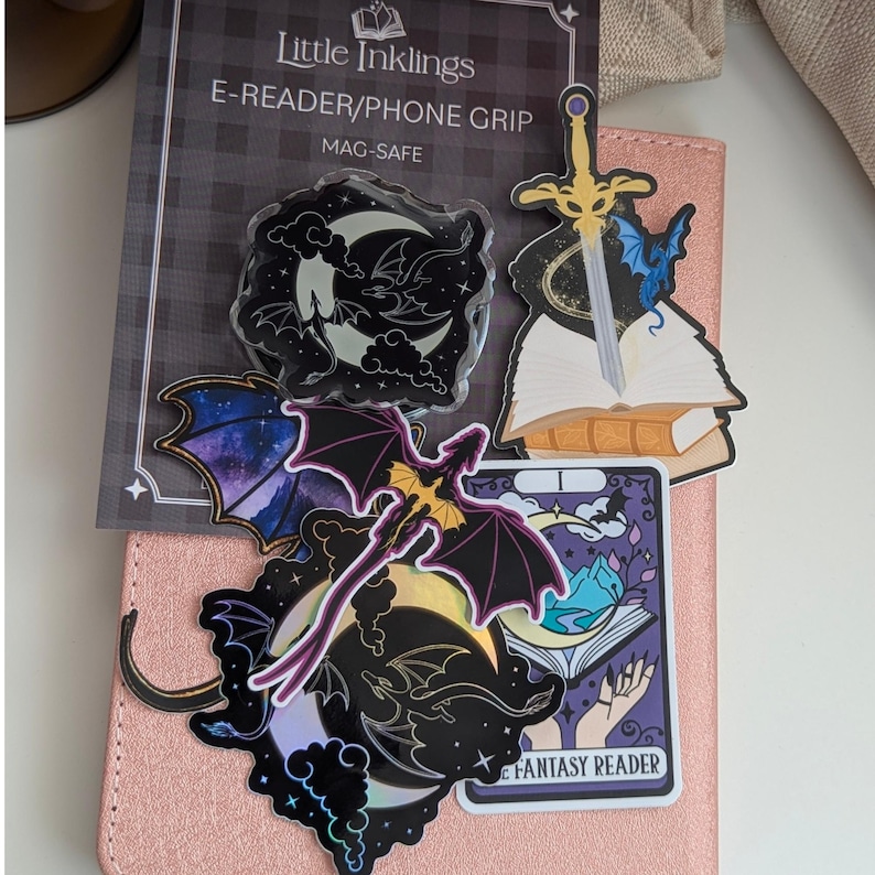 Moon and Dragons Acrylic Kindle Grip. A collection of fantasy-themed stickers and a Mag-Safe e-reader or phone grip on a pink textured surface.