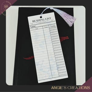 a reading list card with a tassel attached, placed on top of a black notebook or binder.