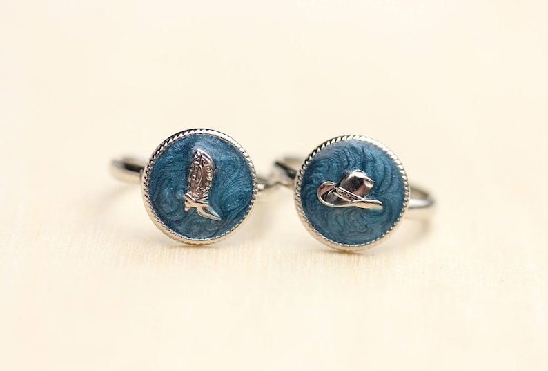 Peut inclure: Deux bagues en argent avec &eacute;mail bleu et un motif de botte de cowboy et de chapeau en argent.