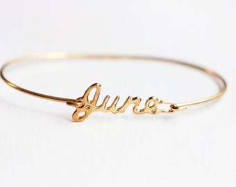 May include: A gold-toned bangle bracelet with the name "June" written in cursive script.