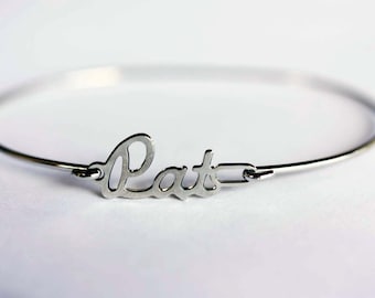 May include: A silver bangle bracelet with the name "Pat" written in a cursive font.