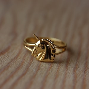 May include: A gold ring featuring a unicorn head design. The unicorn's head is facing left and has a horn.