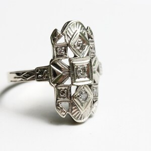 May include: A silver ring with a geometric design and multiple small diamonds.