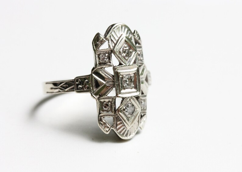 May include: A silver ring with a geometric design and multiple small diamonds.