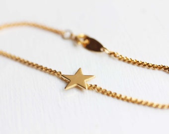 Puede incluir: Un brazalete de cadena dorada con un dije de estrella. La cadena es de estilo cuerda trenzada.
