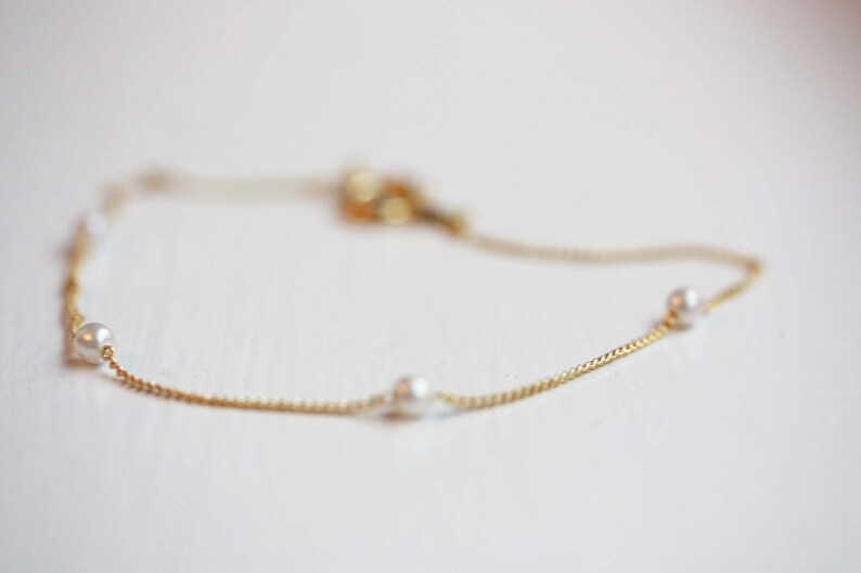 May include: A delicate gold chain bracelet with four small white pearls.