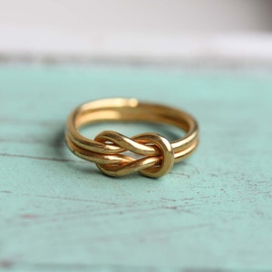Puede incluir: Un anillo de nudo de oro con un diseño simple. El anillo está hecho de dos bandas de metal que se retuercen juntas para formar un nudo.