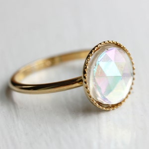 May include: A gold ring with a large iridescent gemstone set in a gold bezel. The gemstone is faceted and has a rainbow of colors.