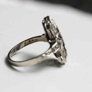 May include: A silver ring with a geometric design set with clear stones. The ring is marked with the number "925" on the inside band.