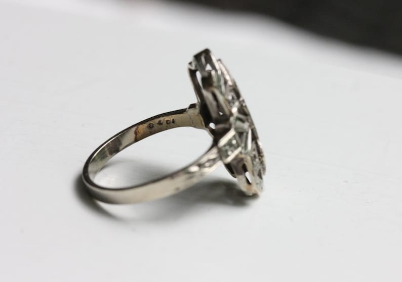 May include: A silver ring with a geometric design set with clear stones. The ring is marked with the number "925" on the inside band.