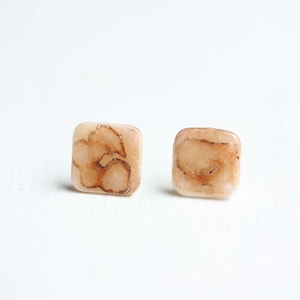May include: A pair of square-shaped earrings with a light brown and white marbled design.