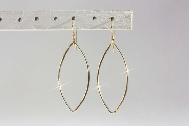 May include: A pair of gold-toned earrings with a teardrop shape. The earrings are made of thin wire and have a simple, elegant design.