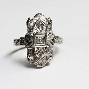 May include: A silver ring with a geometric design and five small diamonds.