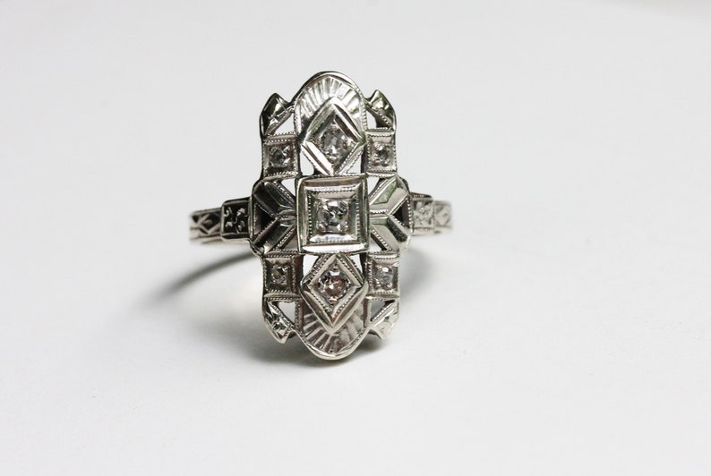 May include: A silver ring with a geometric design and five small diamonds.