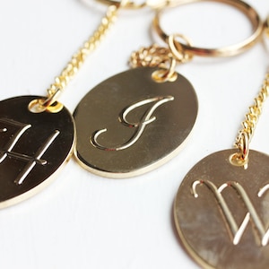 May include: Three gold keychains with round and oval-shaped tags featuring the letters H, J, and W in a cursive font.