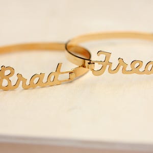 以下が含まれることがあります： 「Brad」と「Fred」という名前が刻まれた2つの金のブレスレット