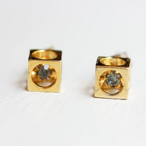 May include: A pair of gold cube earrings with a small clear rhinestone in the center of each cube.