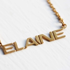 May include: A gold chain necklace with a nameplate pendant that reads "ELAINE".