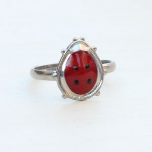 May include: A silver ring with a red ladybug design. The ladybug has black spots and is set in a silver oval.