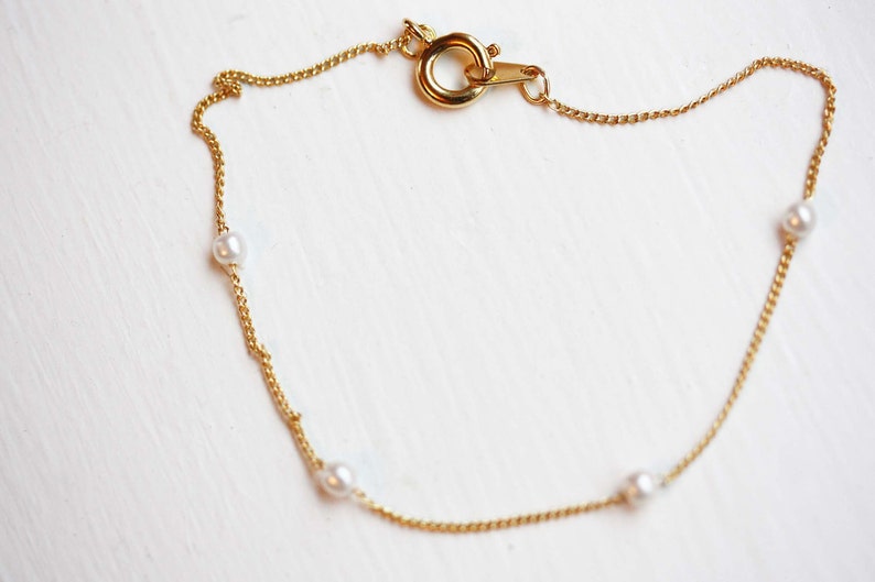 May include: A delicate gold chain bracelet with four small white pearls.