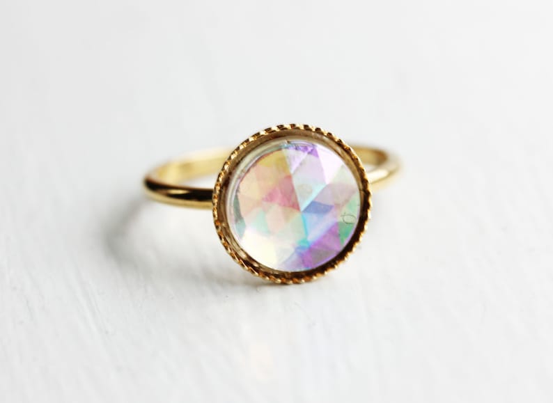 May include: A gold ring with a large iridescent gemstone set in a bezel setting.