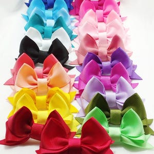 Può includere: Una collezione di 15 fiocchi per capelli colorati in una varietà di colori tra cui rosso, rosa, blu, verde, giallo, arancione, viola e bianco. I fiocchi sono realizzati in nastro di raso e sono fissati a clip per alligatore.