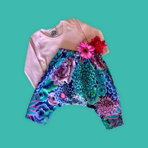 May include: A pink long-sleeved shirt with a floral print and a pair of blue and purple floral print pants. The pants have a wide leg and a gathered waist.