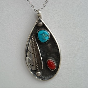 May include: A silver pendant with a turquoise and coral stone inlay. The pendant is shaped like a teardrop and has a silver chain.